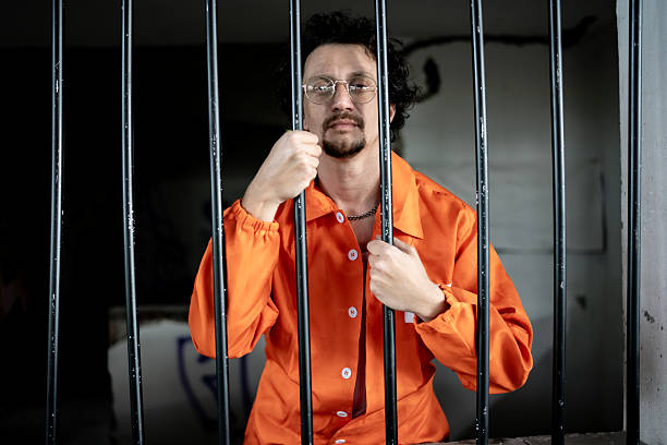 A male inmate wearing an orange uniform stands behind bars in a prison setting, symbolizing incarceration and justice.
