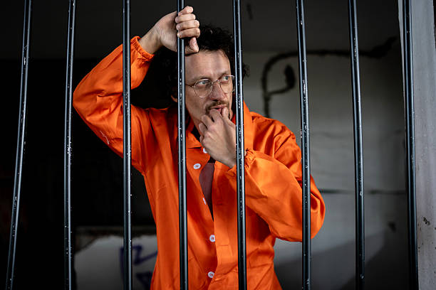 istock Man in Orange Prison Attire Behind Bars Contemplating His Current Situation 2218010135