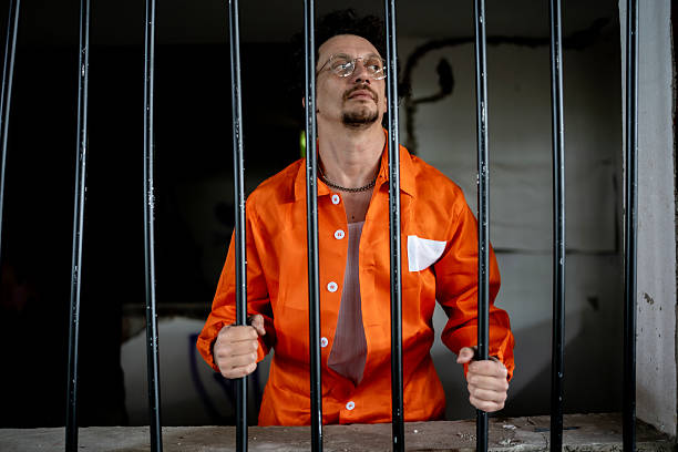 istock Man Detained Behind Bars Wearing Orange Jumpsuit in a Prison Setting 2218010140
