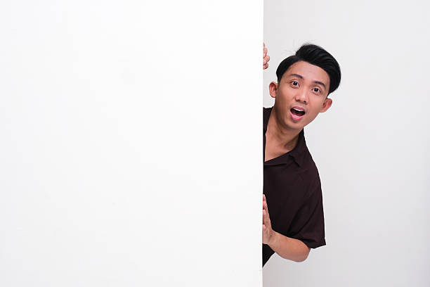 istock Young Asian man peeking behind blank board with surprised expression 2218028967