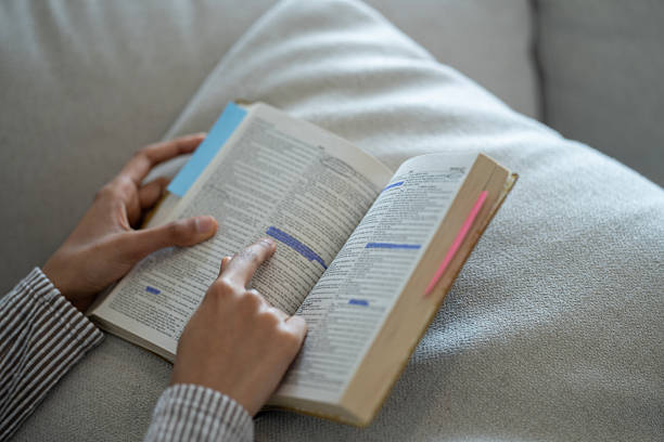 istock Close-Up of Hands Reading a Marked Book on Comfortable Couch 2218039937