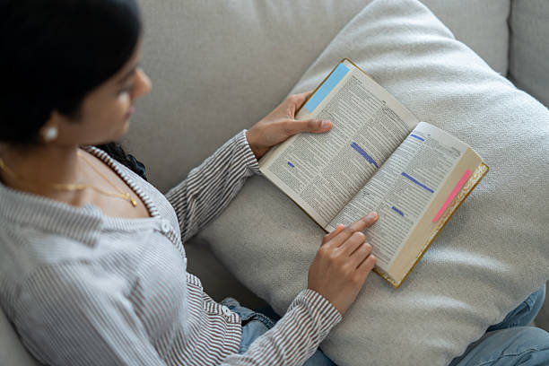 istock Woman Reading a Highlighted Book While Relaxing on a Couch 2218039939