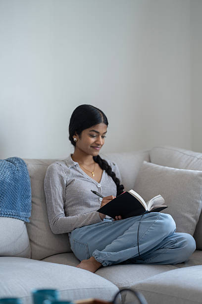 istock Young Woman Relaxing on Couch and Writing in Notebook at Home 2218040491