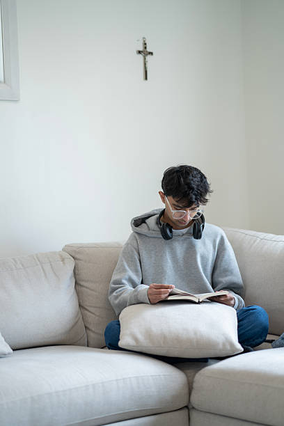 istock Young Person Reading on a Couch with a Cross on the Wall 2218042059