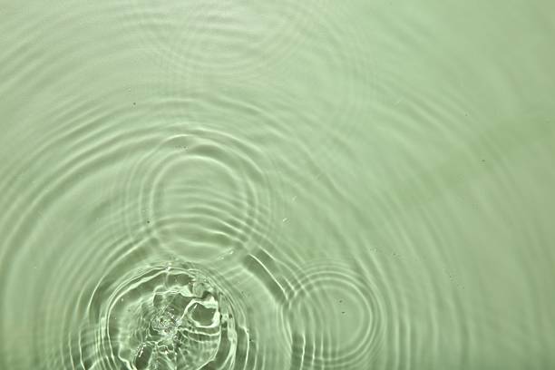Close up macro color image depicting a colorful water drop splashing into a body of water, with ripples. Room for copy space.