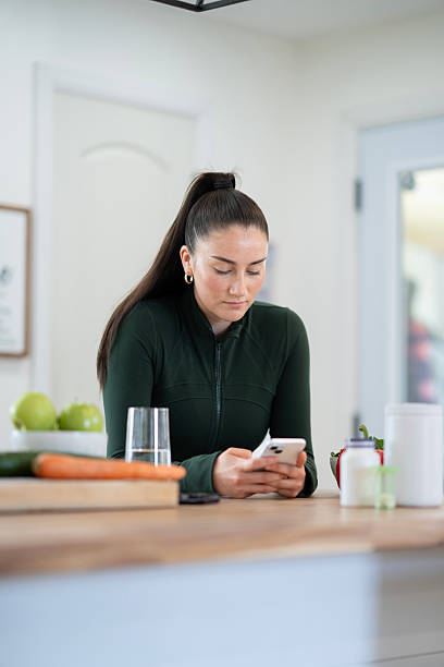 Woman Using Smartphone in Kitchen with Healthy Food Items on Counter
