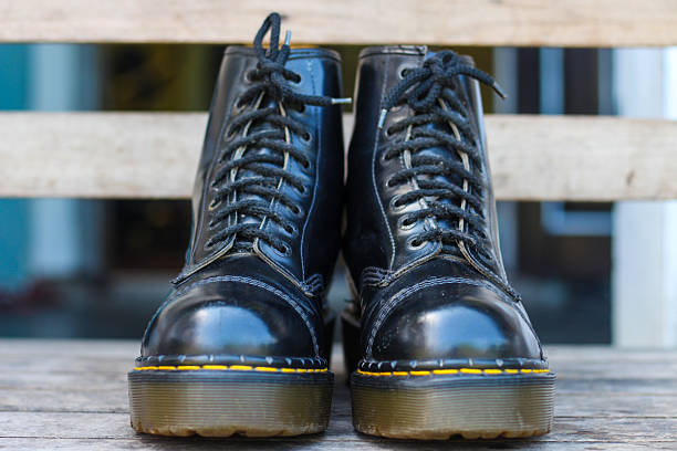Vintage Black Leather Combat Boots on Wooden Surface. A pair of worn black leather combat boots, placed on a wooden bench.