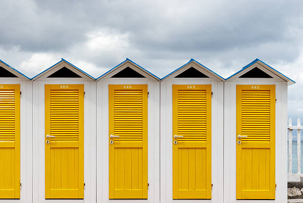 A pretty Asian woman is standing in front of the colorful wooden changing shacks located on Muizenberg Beach in Cape Town, South AFrica. Shot in April 2017, in Fall.