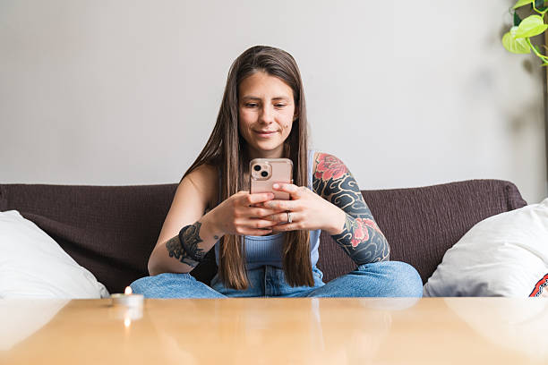 istock Young woman with tattoos using smartphone on sofa at home 2218073389
