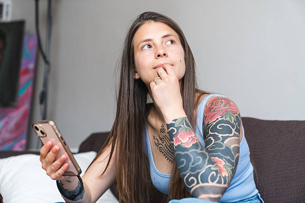istock Pensive young woman with tattoos using smartphone at home 2218073401