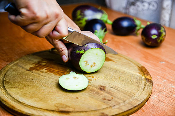 A chef holds a plate of dark eggplants in a rustic setting.