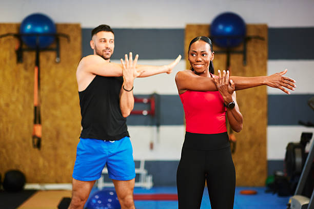 Small group of sporty people in sportswear doing side stretching while sitting on the gym floor. In background mirror.