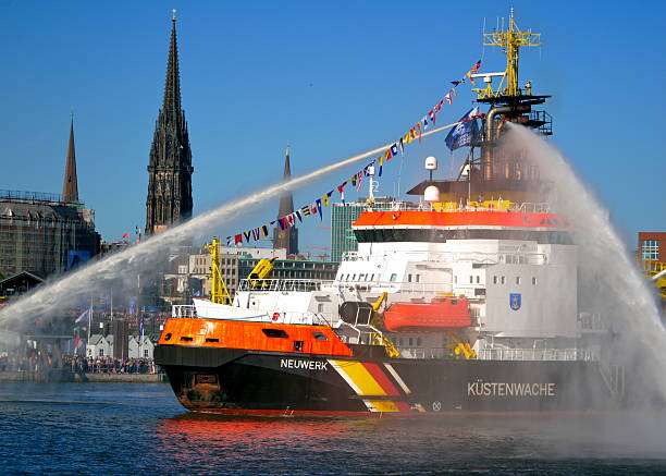 A Coast Guard Vessel Creates Powerful Water Fountains in Front of the Hamburg Skyline, Blending Authority, Motion, and Maritime Spectacle Against an Iconic Urban Backdrop