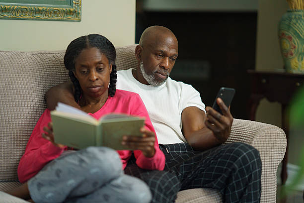 Couple Relaxing at Home, Reading a Book and Using a Smartphone