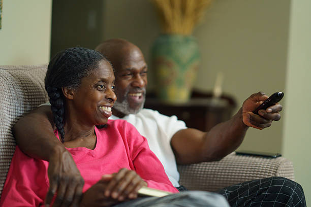 A happy couple enjoys quality time together on the couch, smiling warmly and watching television in their cozy home setting, symbolizing love, togetherness, and relaxation in everyday life.
