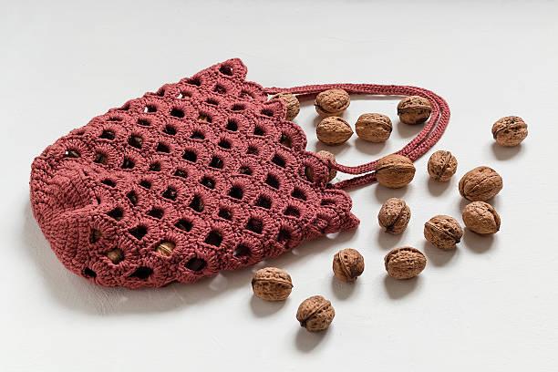 Burgundy crochet bag with round bottom and shell pattern. Market bag with organic walnuts on a white background.