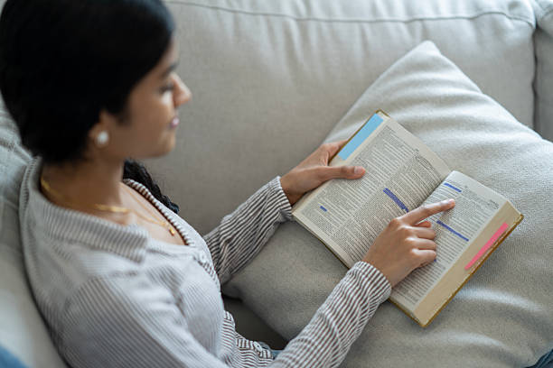istock Young Woman Reading and Highlighting a Textbook While Relaxing at Home 2218103655