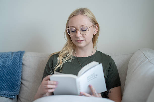 istock Young Woman Reading a Book and Relaxing on a Comfortable Sofa 2218103934