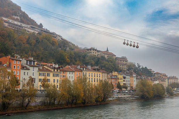Scenic view of cable cars crossing over the historic buildings and lush hillsides of Grenoble, France.