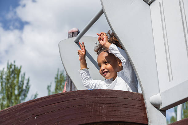 Young girl having fun on a playground structure, raising her hands in the air.