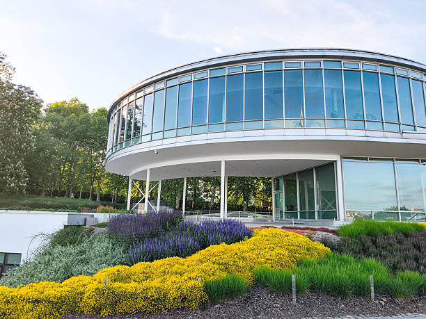 Prague, Czech republic - May 6, 2025: Modern circular building with glass facade standing in letna park in prague, czechia, surrounded by colorful flowers and lush greenery