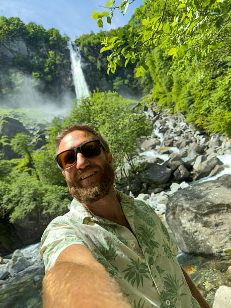 istock Smiling Man Taking a Selfie Near a Waterfall in Lush Forest 2218120539