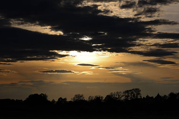 istock A dramatic sunset with dark grey clouds allowing golden light rays to pass through, illuminating silhouettes of trees and buildings. The image conveys the majesty of nature and a unique atmospheric moment. 2218121433