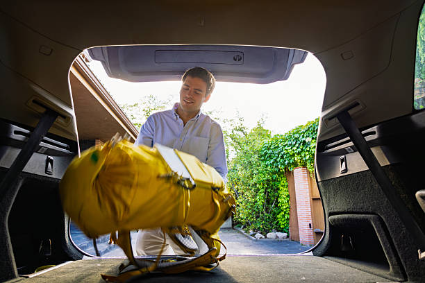 Young tourist loading luggage into car trunk getting ready for road trip adventure