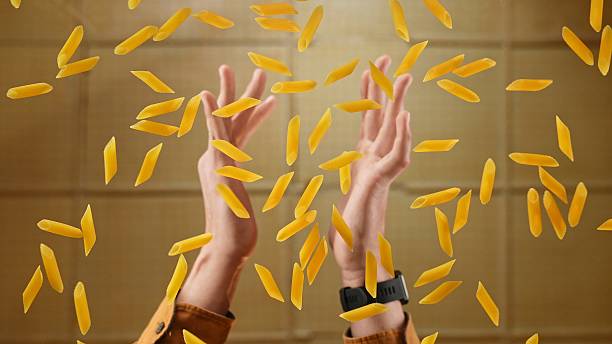 Hands Reaching for Falling Penne Pasta Below the Glass Table