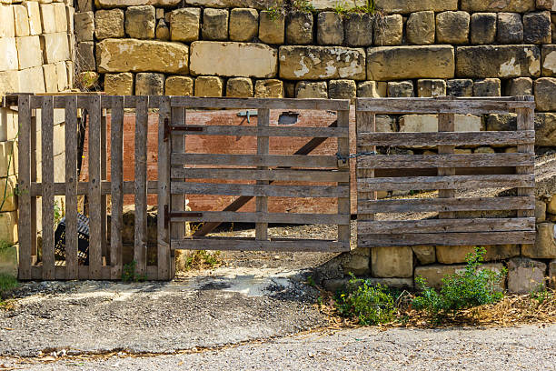 A handcrafted wooden gate in front of an aged stone wall symbolizes countryside charm. The scene embodies rustic craftsmanship and agricultural simplicity, evoking themes of rural life and tradition.