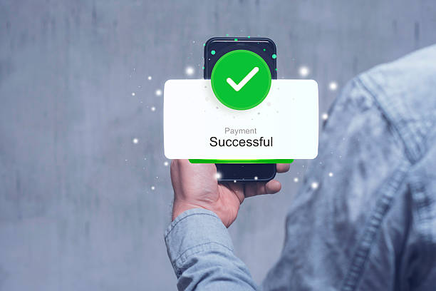 istock A Man in a denim sleeve holds a smartphone displaying a Payment Successful notification with a green checkmark against a blurred background. 2218135232