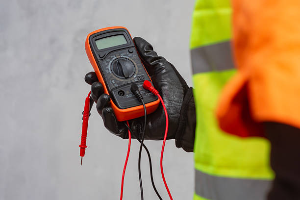 istock Electrician wearing a protective glove, holding a digital multimeter. Orange colored instrument with connected test leads for measuring voltage, current and resistance in electrical systems. 2218136401