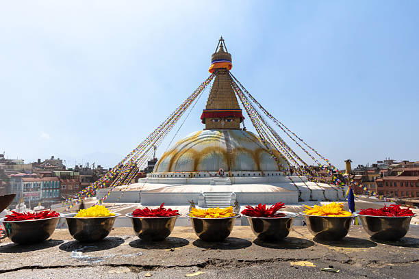 Boudhanath Stupa in Kathmandu, Nepal with flower offerings in foreground. Bright daylight and clear sky.