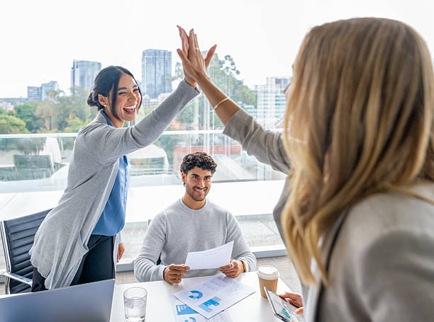 istock Business team members giving each other a high five celebration. There are laptops and paperwork on the board room table showing finance and stock market charts graphs and data 2218149169