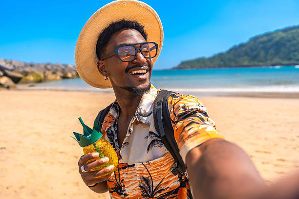 istock Young man taking a selfie on a tropical beach while holding a pineapple-shaped cocktail 2218150631