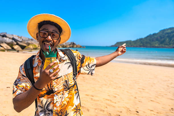 istock Young man drinking a cocktail and pointing at the beach 2218150632