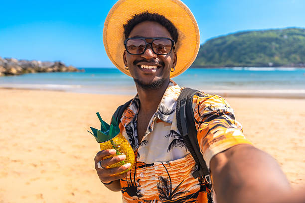 istock Young man taking a selfie on a tropical beach while holding a pineapple cocktail 2218150634