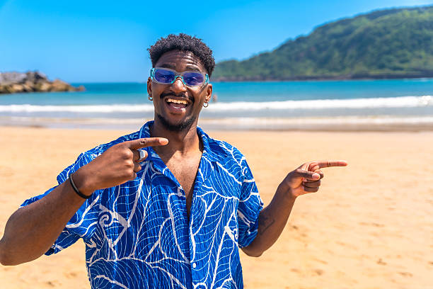 istock Young man pointing sideways with both hands on a tropical beach 2218150651
