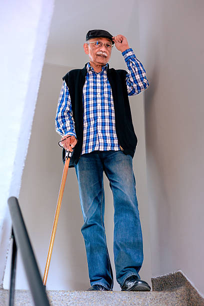 A 77-year-old Asian Indian man is seen arriving from his walk in the corridor outside his apartment. He has just come up the stairs to his left. He is using a cane for support because he suffers from Vertigo. Image shot indoors in a section of the staircase, in ambient light.