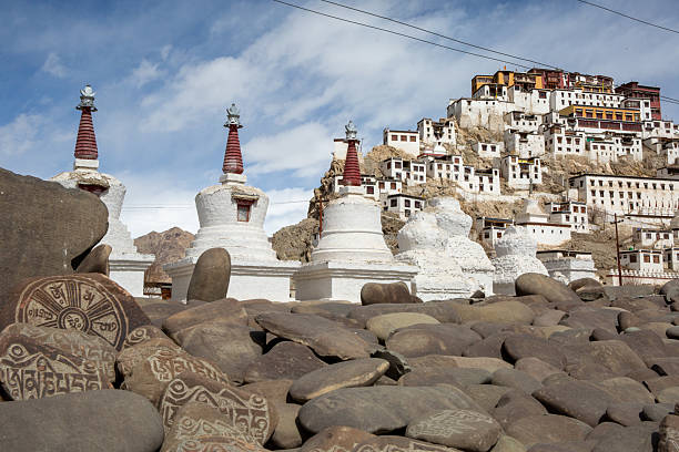 View of Tibetan Buddhist monastery and chortens in Leh, Ladakh, India, with carved stones in the foreground. The structures are situated on a hill with clear sky in the background.