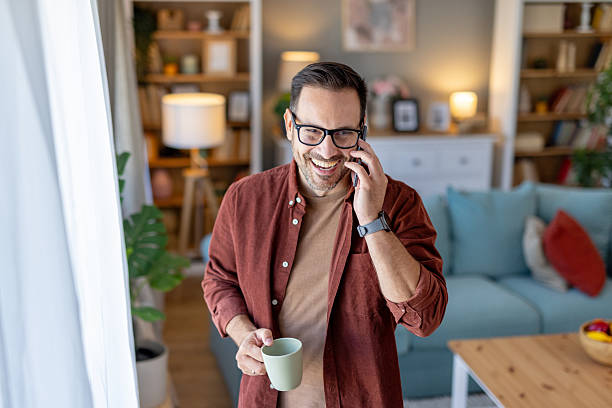 istock Man Laughing on Phone with Coffee in Bright Living Room 2218155487
