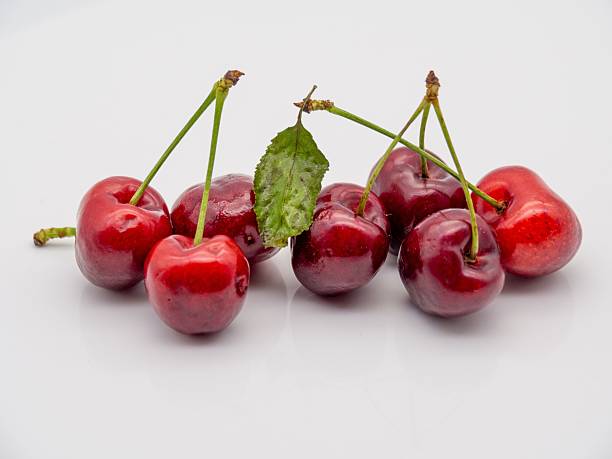 The fresh red cherries with stems and a leaf on a white background, showcasing vibrant colors