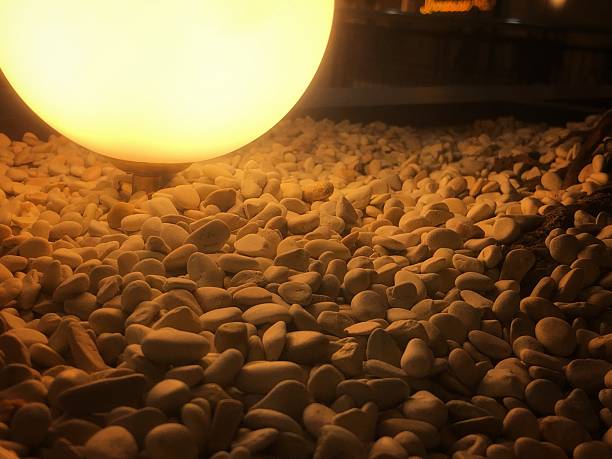 A warm, glowing spherical lamp illuminates a bed of light-colored river pebbles, creating a serene and inviting ambiance. This outdoor lighting design is perfect for pathways, gardens, or decorative accents at night.