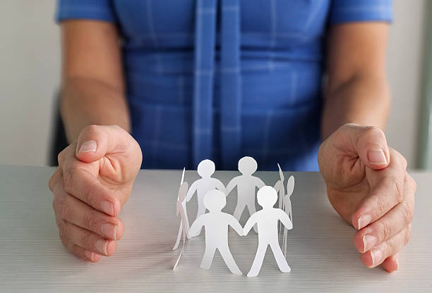 Two hands gently cradle a circle of paper cutout figures representing community support and togetherness, symbolizing unity and collaboration among individuals concept