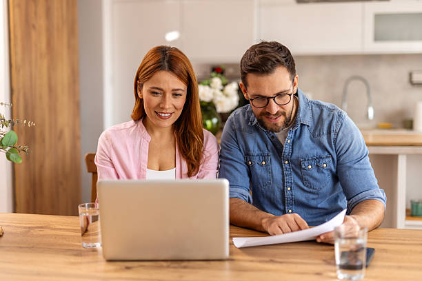 istock Couple is sitting at a table, focused on a laptop screen. They be discussing or working together, highlighting themes of collaboration, technology, and modern lifestyle in a home office setting 2218187485