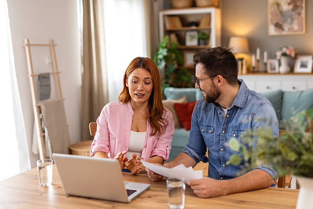 istock Couple is sitting at a table, focused on a laptop screen. They be discussing or working together, highlighting themes of collaboration, technology, and modern lifestyle in a home office setting 2218187489