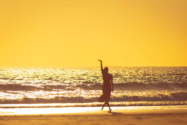 Woman dancing on the beach at golden sunset: silhouette of graceful dancer enjoying freedom and tranquility by the ocean