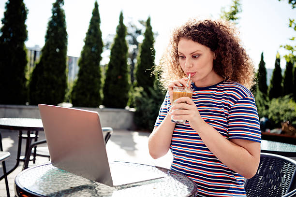 istock Young woman sipping iced coffee while studying outdoors on a sunny day, enjoying leisure time with her laptop. 2218201806