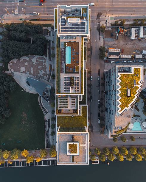 Aerial view of modern urban architecture with green rooftops and a rooftop pool, surrounded by roads and greenery.
