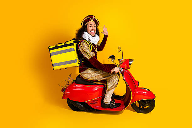 istock Young man dressed as a nobleman delivering on a red scooter against yellow background 2218202836